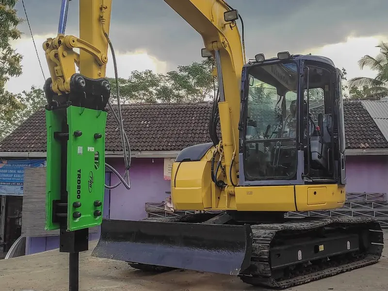 Ekskavator kuning dengan breaker hijau di lengannya