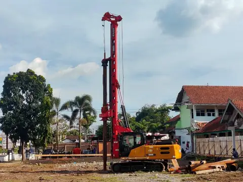 Rig bor bertiang merah dengan dasar kuning di lahan kosong dekat permukiman