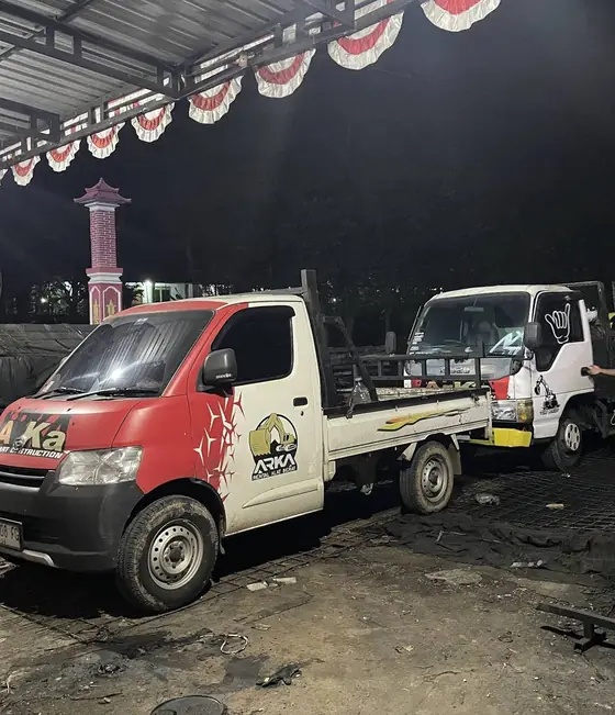 Dua pickup bergambar ARKA di dalam bangunan beratap seng pada malam hari