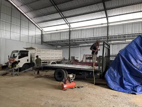Seorang pria di atas bak truk datar di dalam bangunan luas, dengan kompresor di lantai dan truk putih di belakangnya