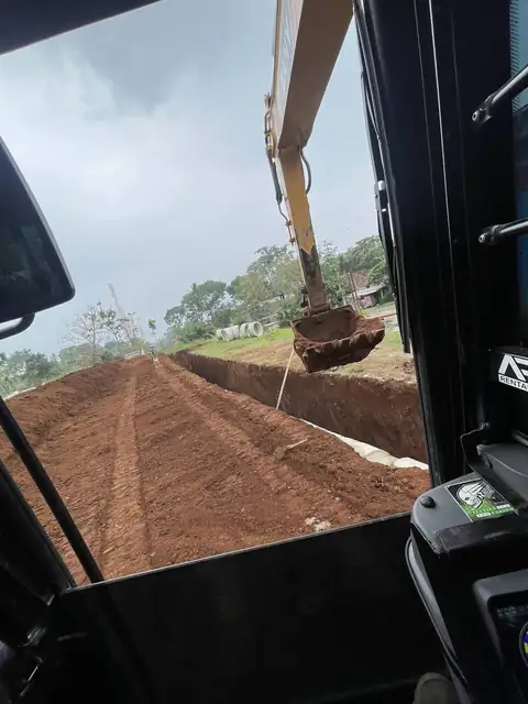 Pemandangan dari dalam kabin, lengan ekskavator di atas tanah merah yang dikeruk berjajar