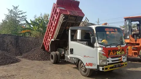 Dump truk ARKA menurunkan muatan di dekat tumpukan material gelap, dengan alat oranye di sebelahnya