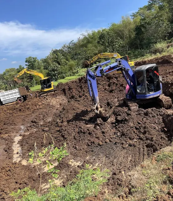 Ekskavator biru dan kuning menggali tanah di lereng