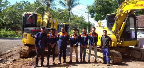 Tujuh orang berseragam berdiri berjajar di depan dua ekskavator kuning