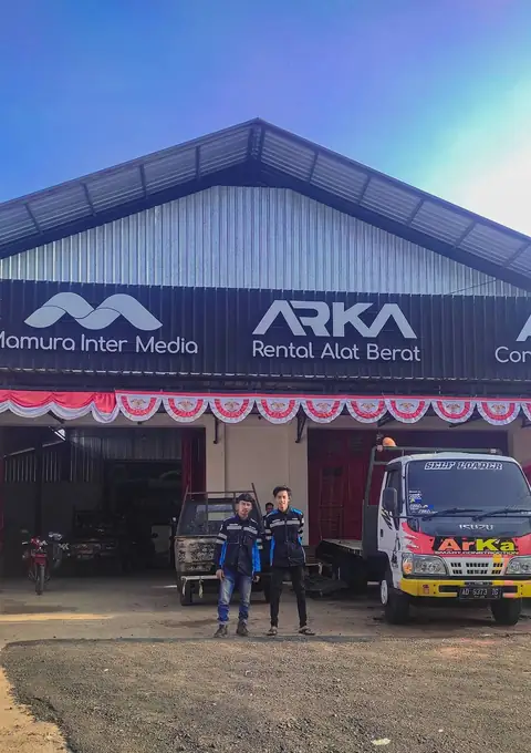 Dua pria berdiri di depan kantor berpapan ARKA Rental Alat Berat, dengan sebuah truk di sebelahnya