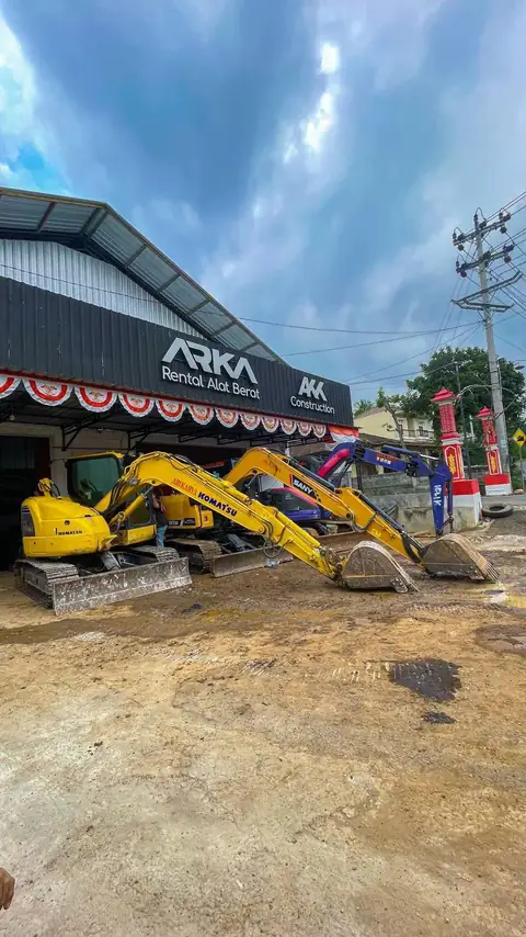 Ekskavator kuning di halaman depan kantor dengan papan nama ARKA
