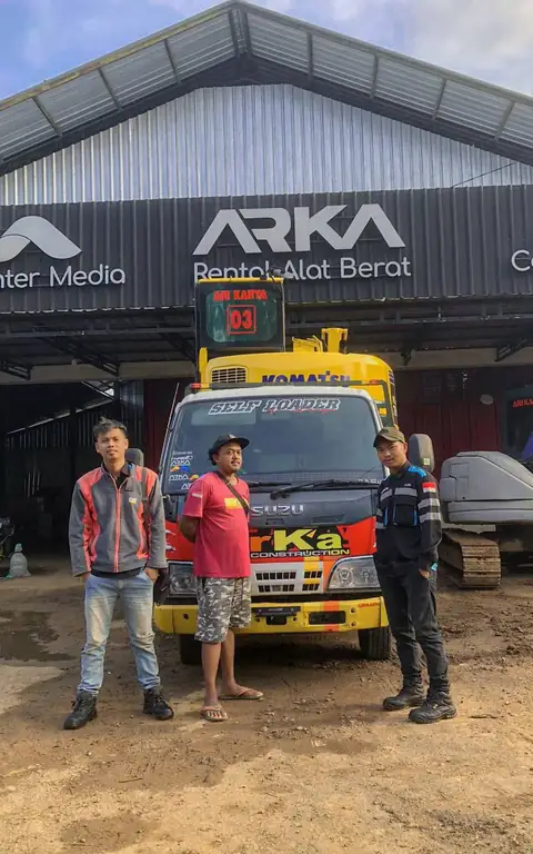 Tiga pria berdiri di depan truk kuning di bawah papan nama ARKA Rental Alat Berat