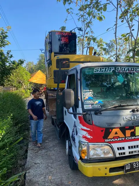 Truk bergambar ARKA membawa alat kuning di baknya, seorang pria berdiri di dekatnya