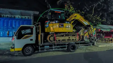 Ekskavator kuning kecil di atas truk kecil pada malam hari