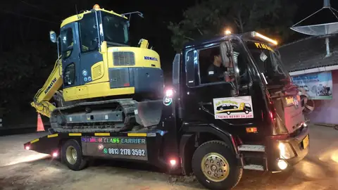 Ekskavator kuning di atas truk pengangkut hitam pada malam hari