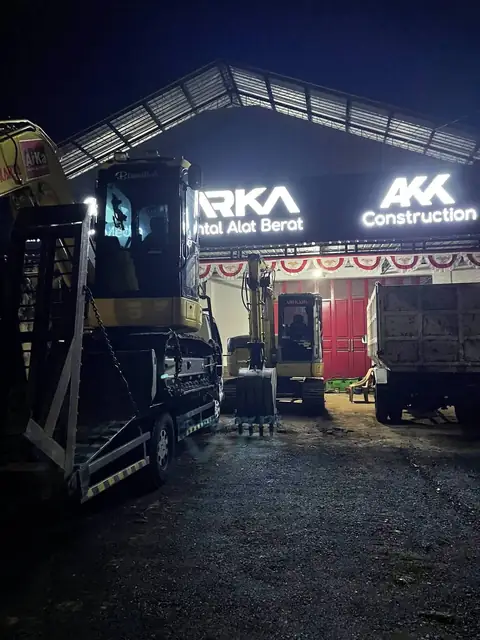 Kantor ARKA pada malam hari dengan papan nama menyala, ekskavator di atas truk di halaman